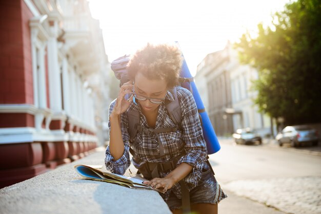 Female traveler with backpack speaking on phone, looking at map.