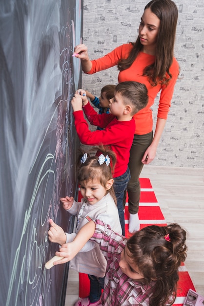 Female tutor drawing on blackboard with kids
