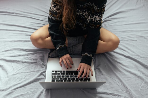 Femmina che digita sul computer portatile mentre era seduto sul letto con le gambe incrociate