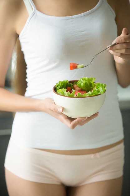 Female in underwear holding a bowl of green salad