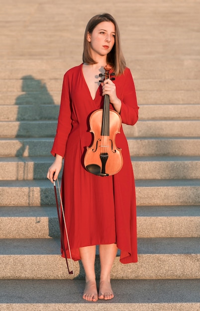 Foto gratuita violinista femminile in posa sui gradini con il violino