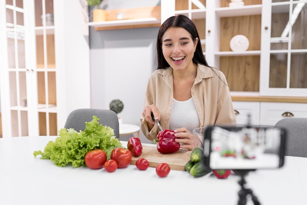 Foto gratuita vlogger femminile a casa con verdure e smartphone