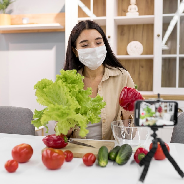 Foto gratuita vlog femminile a casa con maschera medica e verdure