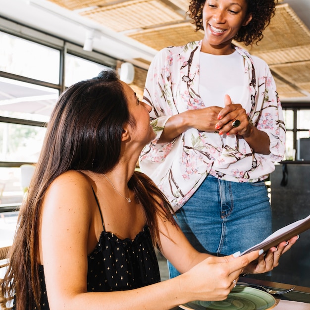 Female waiter taking orders from young woman customer in restaurant