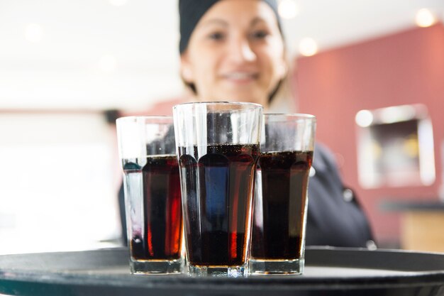 Женская официантка, предлагающая стаканы питья на подносе