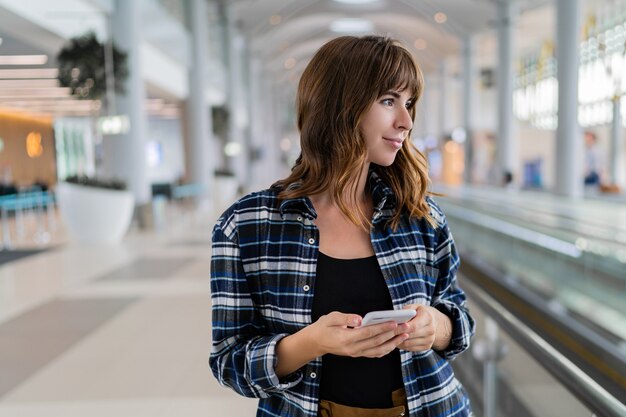 スマートフォンを使って空港を歩いている女性。