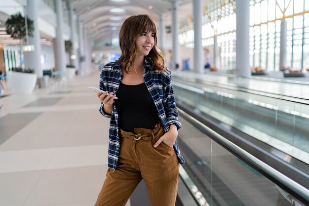 그녀의 스마트 폰 장치를 사용하여 공항을 걷는 여성.