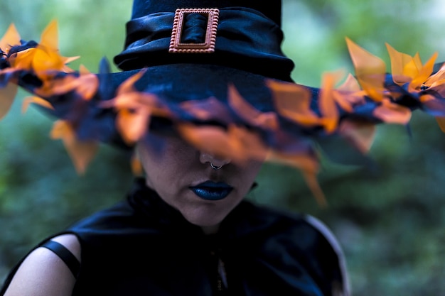 Бесплатное фото Женщина в гриме ведьмы и костюме с украшенной шляпой, запечатленная в лесу