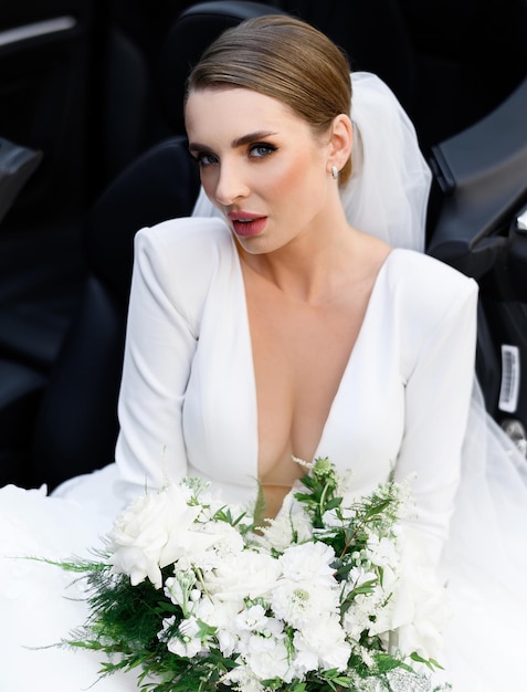 Free photo female in wedding dress with bunch of flowers sitting in cabriolet