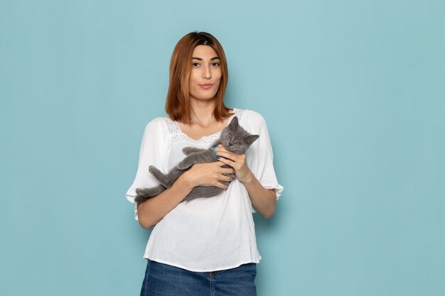 female in white blouse and blue jeans holding grey kitten