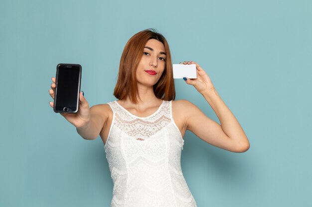 female in white blouse and blue jeans holding phone and card