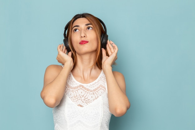 female in white blouse and blue jeans listening to music