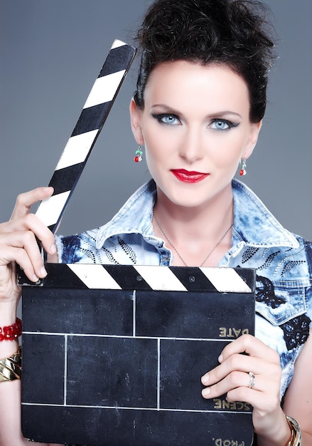 A female with a bright  make up holding  a clapperboard. Isolated on a grey background.