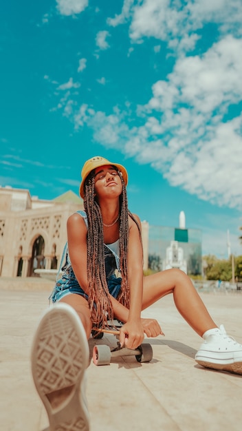 Female with dreadlocks in a bucket hat and with skateboard posing at camera