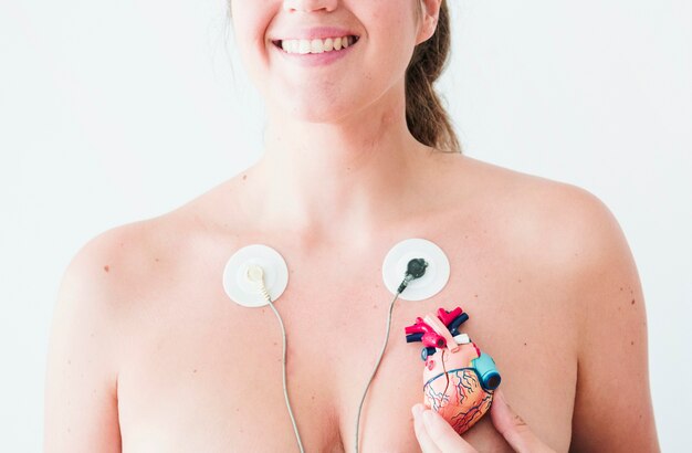 Female with electrocardiogram leads and hand with figurine of heart 