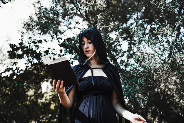 Foto gratuita stregone femminile con libro degli incantesimi nei boschi di giorno