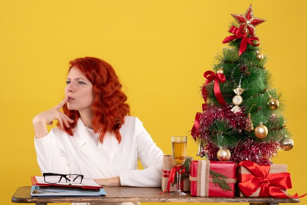 小さなクリスマスツリーと黄色のプレゼントと彼女のテーブルの後ろに座っている女性労働者
