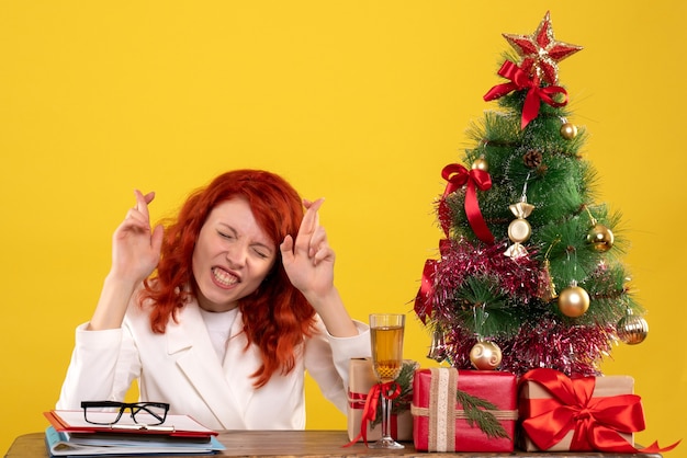 Lavoratrice seduta dietro il tavolo con regali di natale e albero sperando in giallo