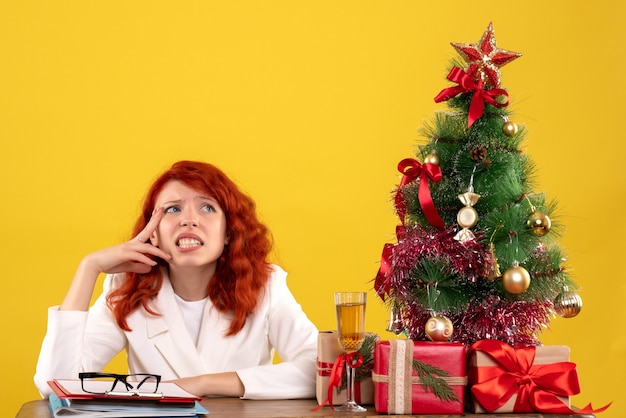 female worker sitting behind table with christmas presents and tree on yellow