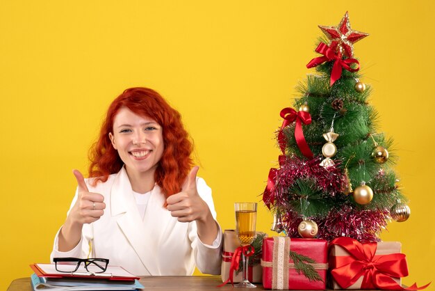 female worker sitting behind table with christmas presents and tree on yellow