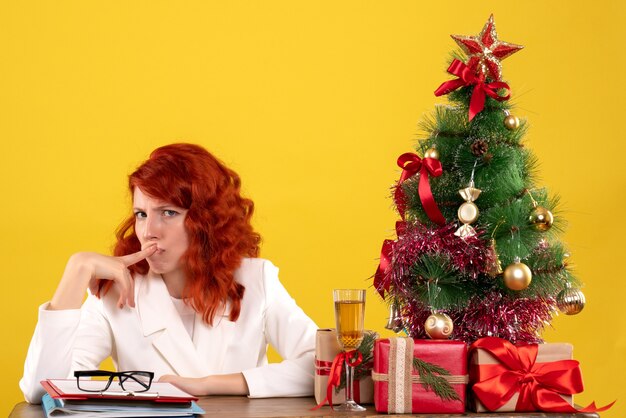 работница сидит за столом с рождественскими подарками и елкой на желтом
