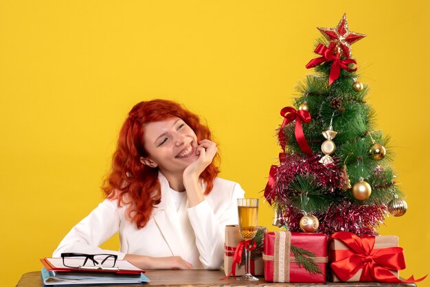 female worker sitting behind table with christmas presents and tree on yellow