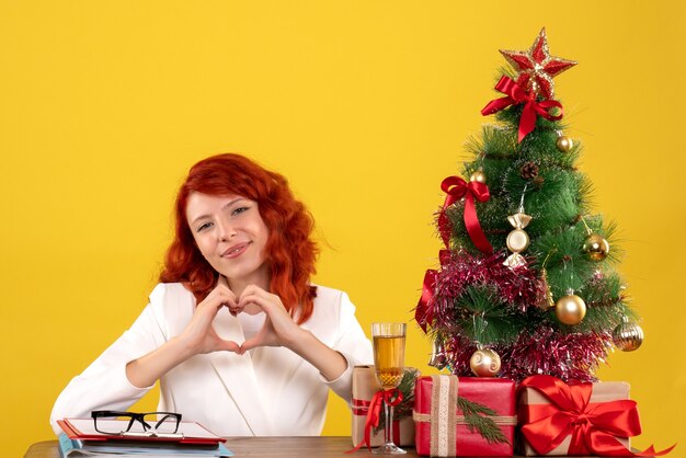female worker sitting behind table with christmas presents and tree on yellow