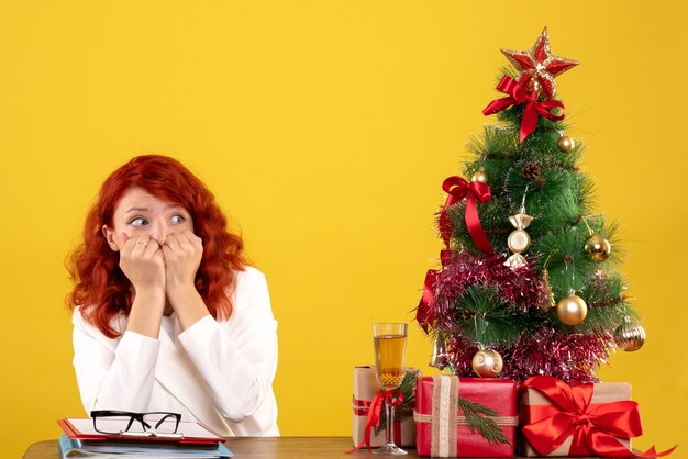 female worker sitting behind table with christmas presents and tree on yellow