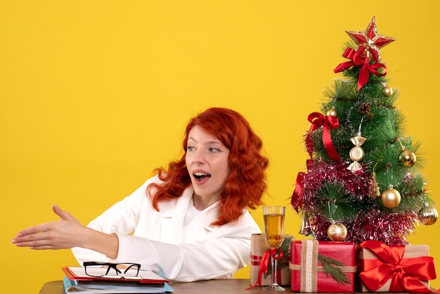 female worker sitting behind table with christmas presents and tree on yellow