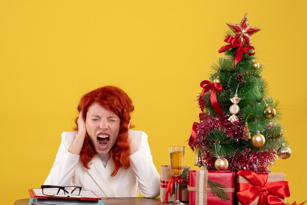 female worker sitting behind table with xmas tree and presents on yellow