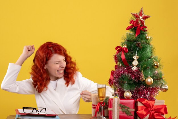 female worker sitting behind table with xmas tree and presents on yellow
