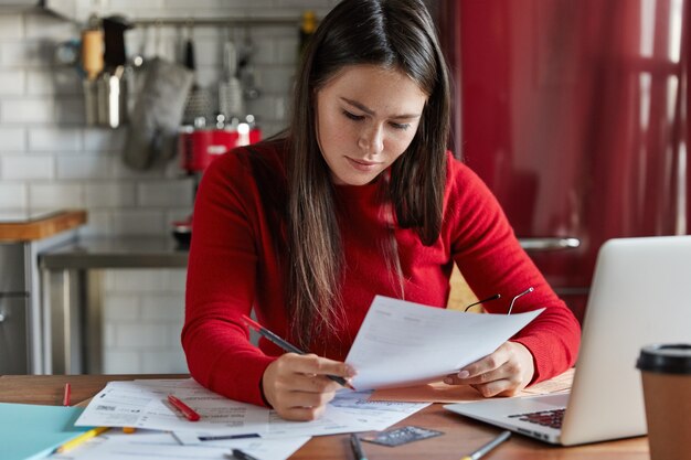 女性労働者は市場分析を研究し、財務予測を行い、文書、電子機器を使って職場でポーズをとり、台所で働きます。