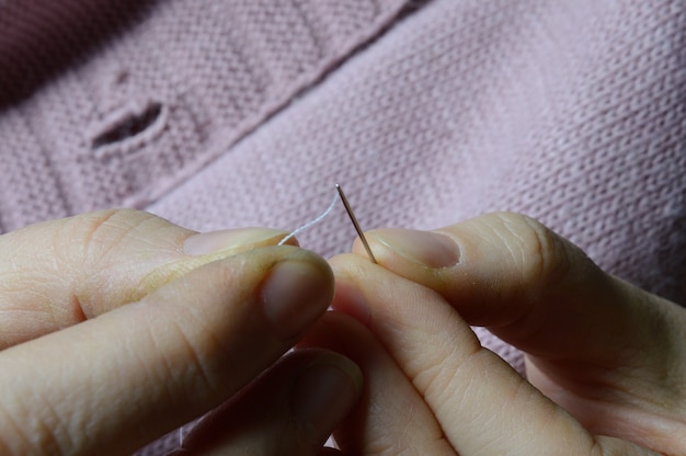 女性​労働者​の​手​が​木製​の​ボタン​を​ジャケット​に​縫い​付けています​。​閉じる​。
