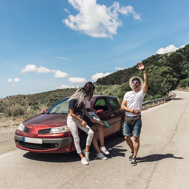 Females leaning on car looking at map while her male friend looking for something