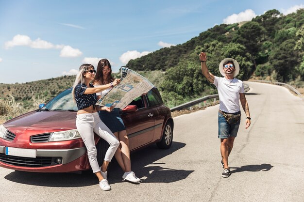 Females looking at map leaning on car while her male friend gesturing on road