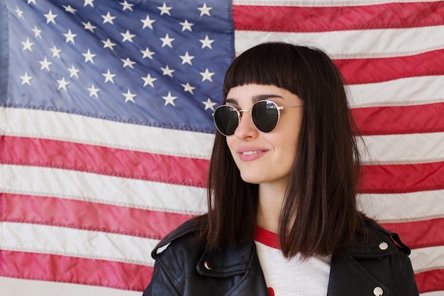 Free photo feminine beautiful woman or teenage girl wears new sunglasses eyewear in front of american flag, trendy and fashionable hipster, patriot of usa