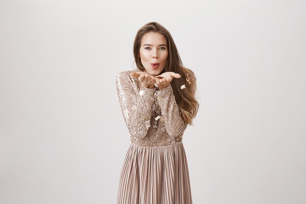 Feminine woman blowing golden confetti in evening dress