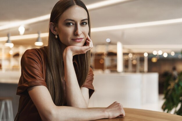 Feminine young alluring woman leaning on coffee table sitting in cafe looking camera with slight romantic smile gazing sensually having date with boyfriend in favorite place downtown