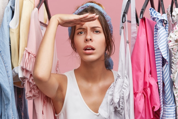 Femlae seller in clothes shop looking into distance while waiting for customers with great desire. Attractive female model doing shopping alone, waiting for her friend to come to give her advice