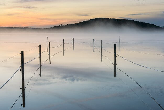 スウェーデン、ラダションの日没時の霧の湖のフェンスで囲まれたパドック