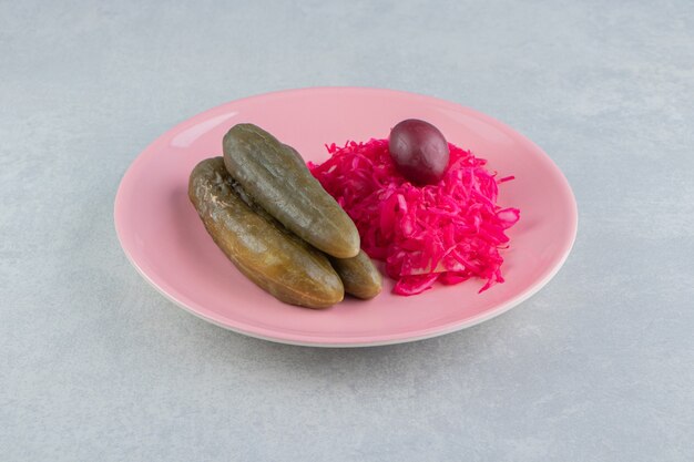 Fermented cucumbers and cabbage on pink plate. 