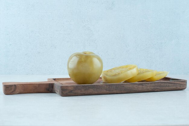 Fermented green tomato slices on wooden board.