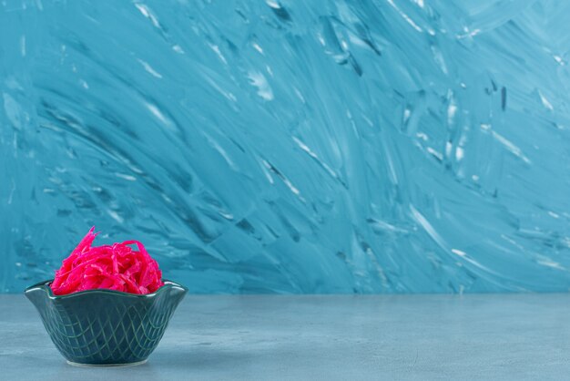 Fermented red cabbage lies in a bowl, on the blue table. 