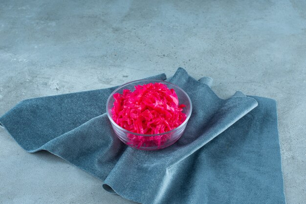 Fermented red cabbage lies in a bowl on piece of fabric, on the blue table. 