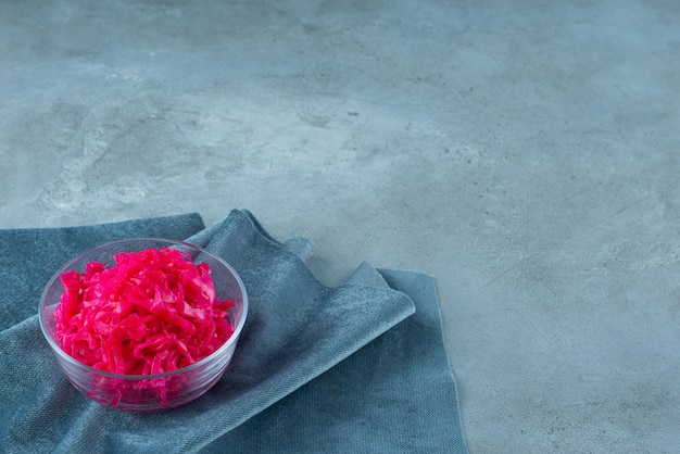 Free photo fermented red cabbage lies in a bowl on piece of fabric, on the blue table.