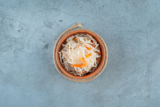 Fermented sauerkraut with carrots in a bowl on a trivet on the blue surface