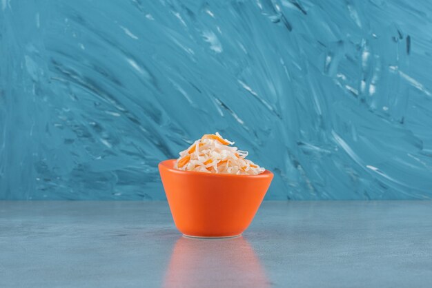 Fermented sauerkraut with carrots in a plastic bowl , on the blue table. 