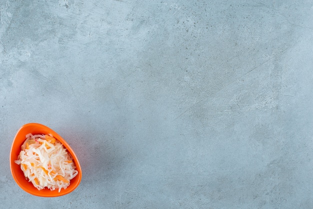 Fermented sauerkraut with carrots in a plastic bowl , on the blue table. 