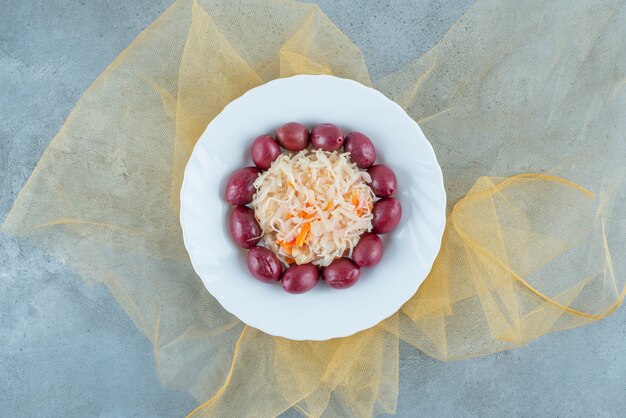 Fermented sauerkraut with plums on a plate on a tulle , on the blue table. 