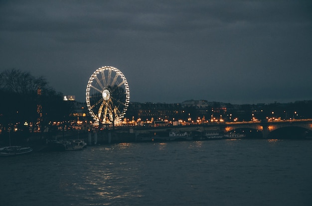 Ferris Wheel surrounded by a river and buildings under a cloudy sky during the night in Paris